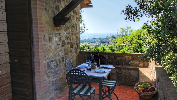 An outdoor patio with a table set for two, stone walls, and a view of the countryside.