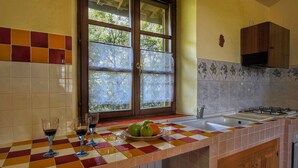 A kitchen with a checkered tile countertop, a window with lace curtains, and a stove.