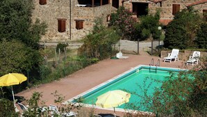 A stone villa with a swimming pool, surrounded by greenery and hills.