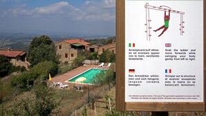 A sign with instructions for using a fitness apparatus, set against a backdrop of a swimming pool and rural buildings.