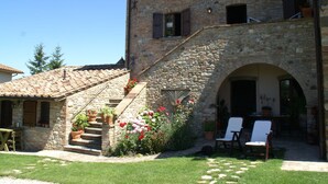 A stone building with a staircase leading to a door, surrounded by a garden with potted plants and flowers. - Holiday Home in Montone With Swimming Pool (Montone)