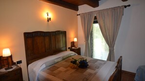 A bedroom with a wooden headboard, a bedside table with a lamp, a window with curtains, and a floral arrangement on the bed. - Belvilla by OYO Il Gelso (Modigliana)