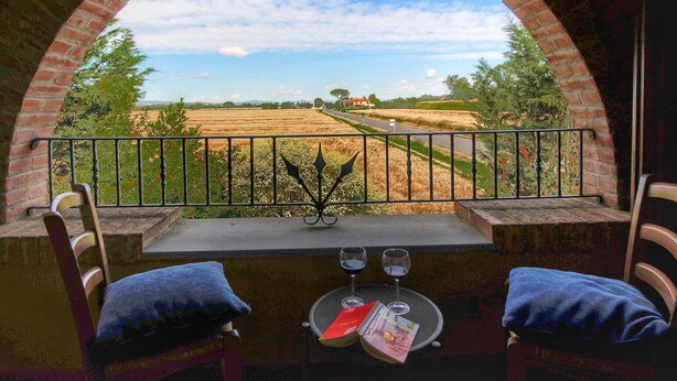 A balcony with a view of a rural landscape, two chairs, and a table with glasses and magazines. - Tuscan Retreat With Pool (Cortona)