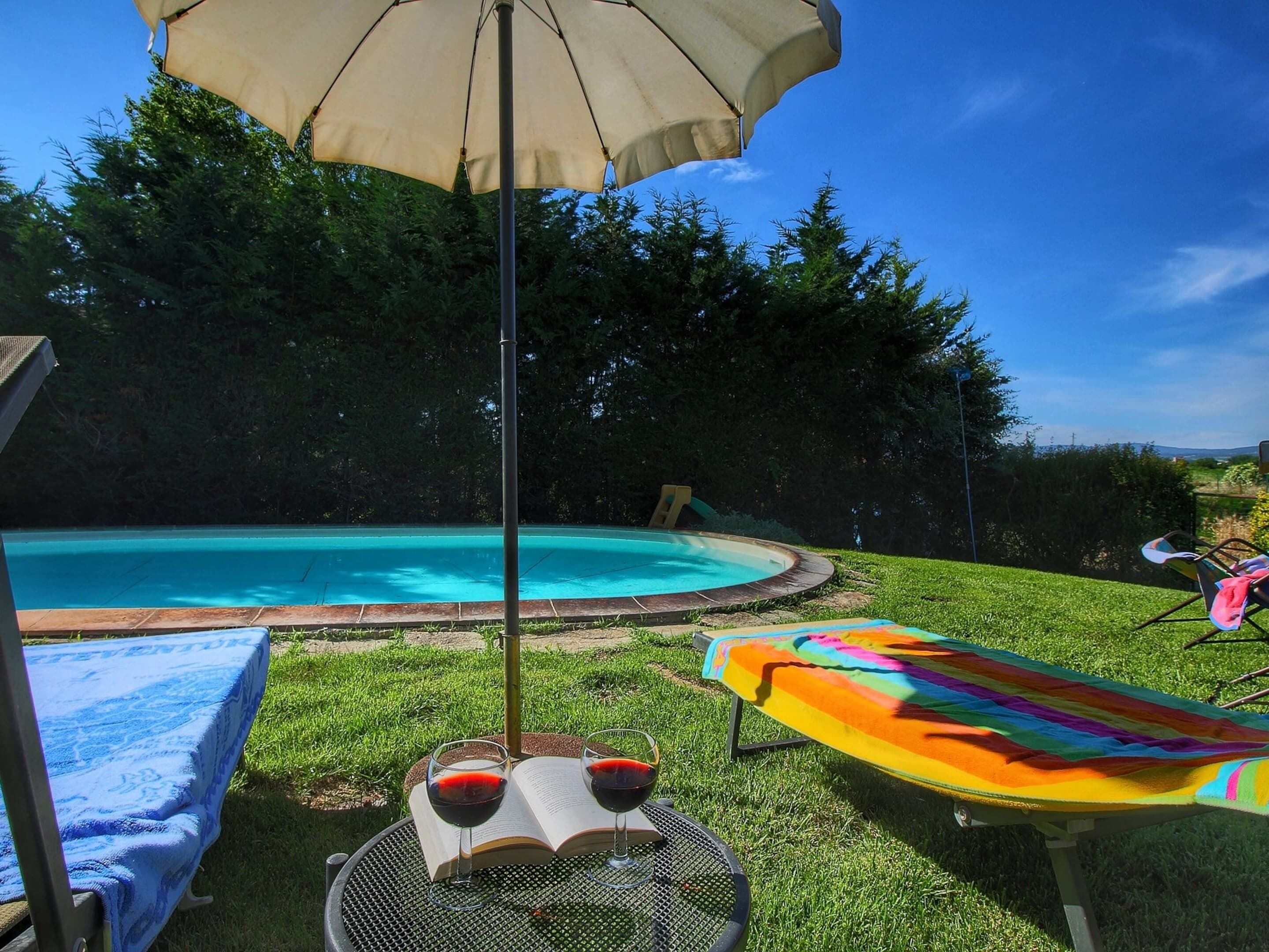 Ein Garten mit Swimmingpool, einem überdachten Tisch mit Getränken und einem bunten Strandtuch.