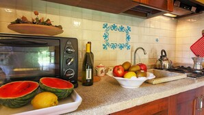 A kitchen with a microwave, a bowl of fruit, a wine bottle, and a kettle. - Tuscan Retreat With Pool (Cortona)