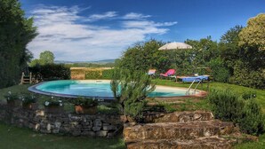 A circular pool with a stone wall and potted plants, surrounded by a lush garden and a view of distant hills. - Tuscan Retreat With Pool (Cortona)