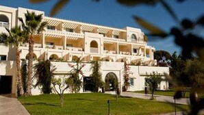 A multi-story hotel with a white facade, multiple balconies, and a well-maintained lawn with palm trees. - Comfy Apartment with Balcony near Puglia Beach (Ostuni)