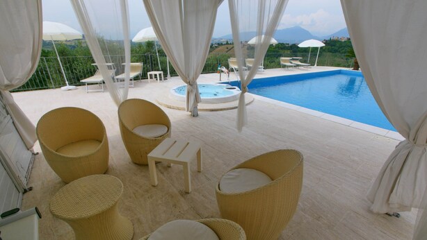 A poolside area with wicker furniture and a hot tub, overlooking a mountainous landscape.