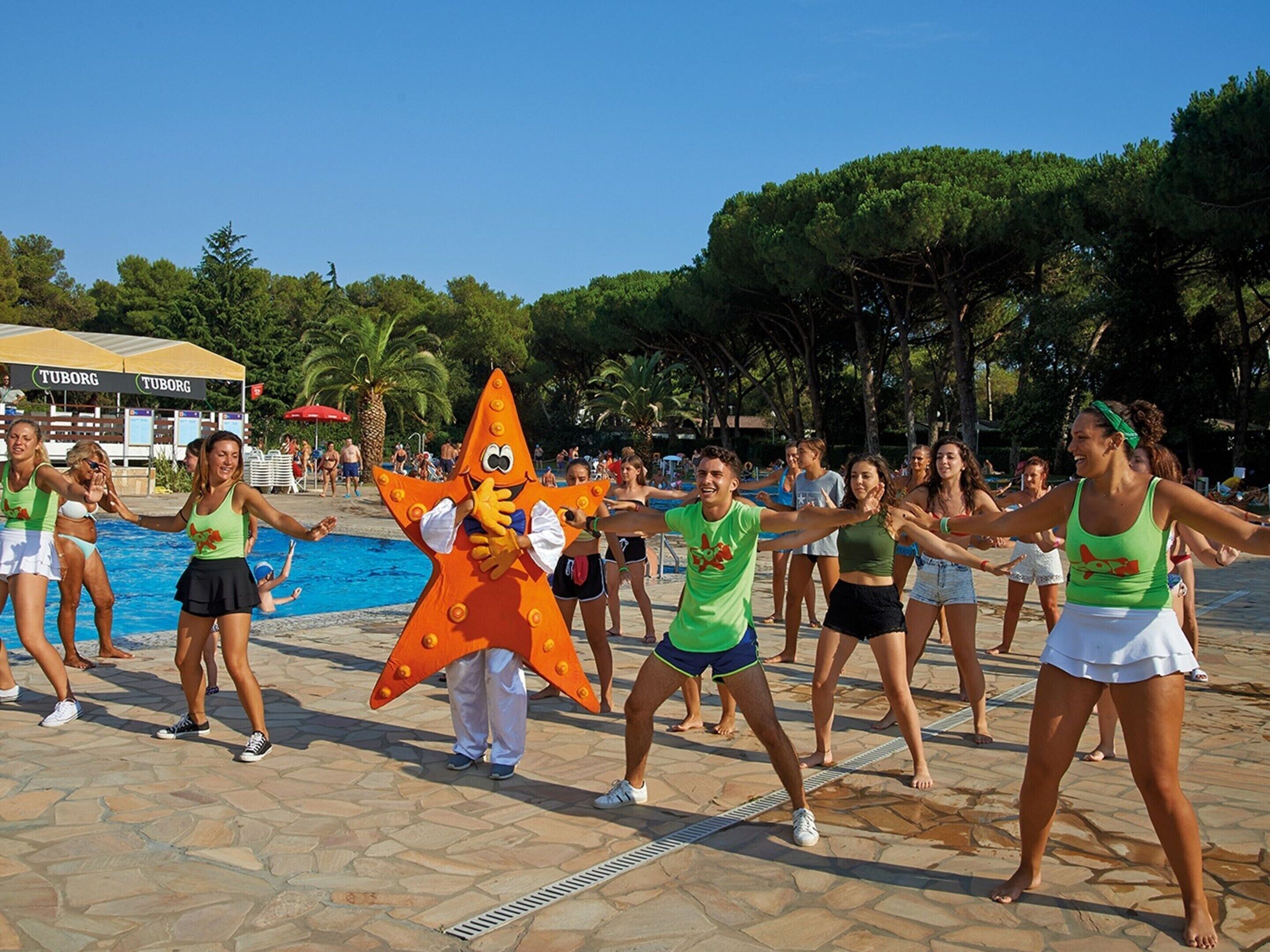 Um grupo de pessoas fazendo exercícios ao ar livre perto de uma piscina, com um personagem inflável grande no centro.