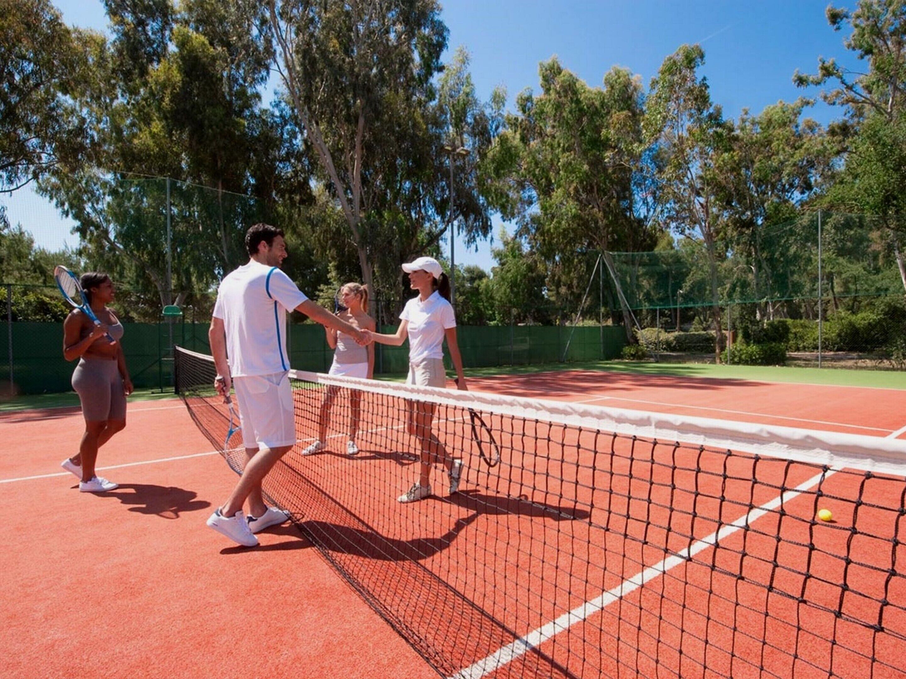 A tennis court with four people, one holding a racket, and a tennis ball on the ground.