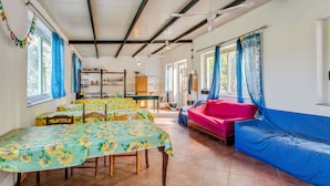 A room with a dining table, two beds, a sofa, and a kitchen area.