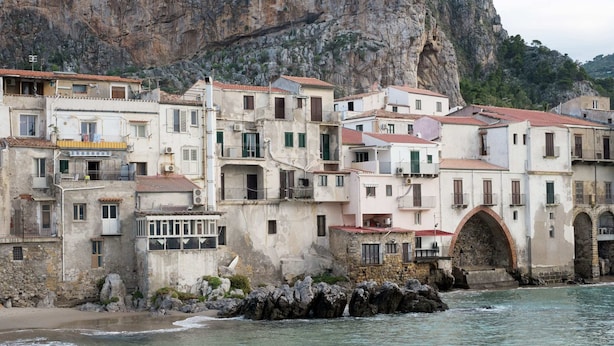 A coastal town with multi-story buildings, a rocky cliff, and a beach.