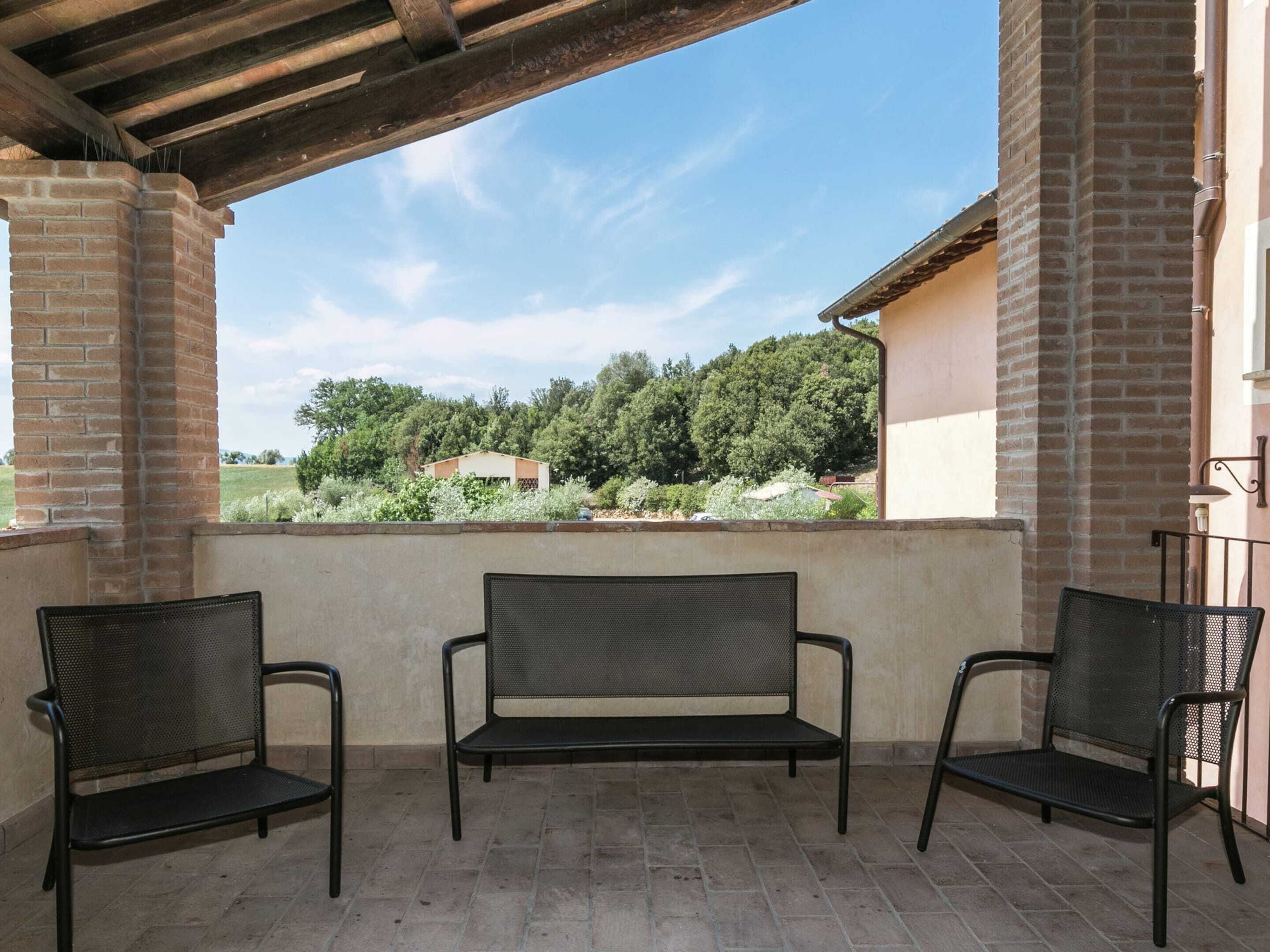 Eine überdachte Terrasse mit einer Backsteinmauer, zwei schwarzen Metallstühlen und einer Bank.