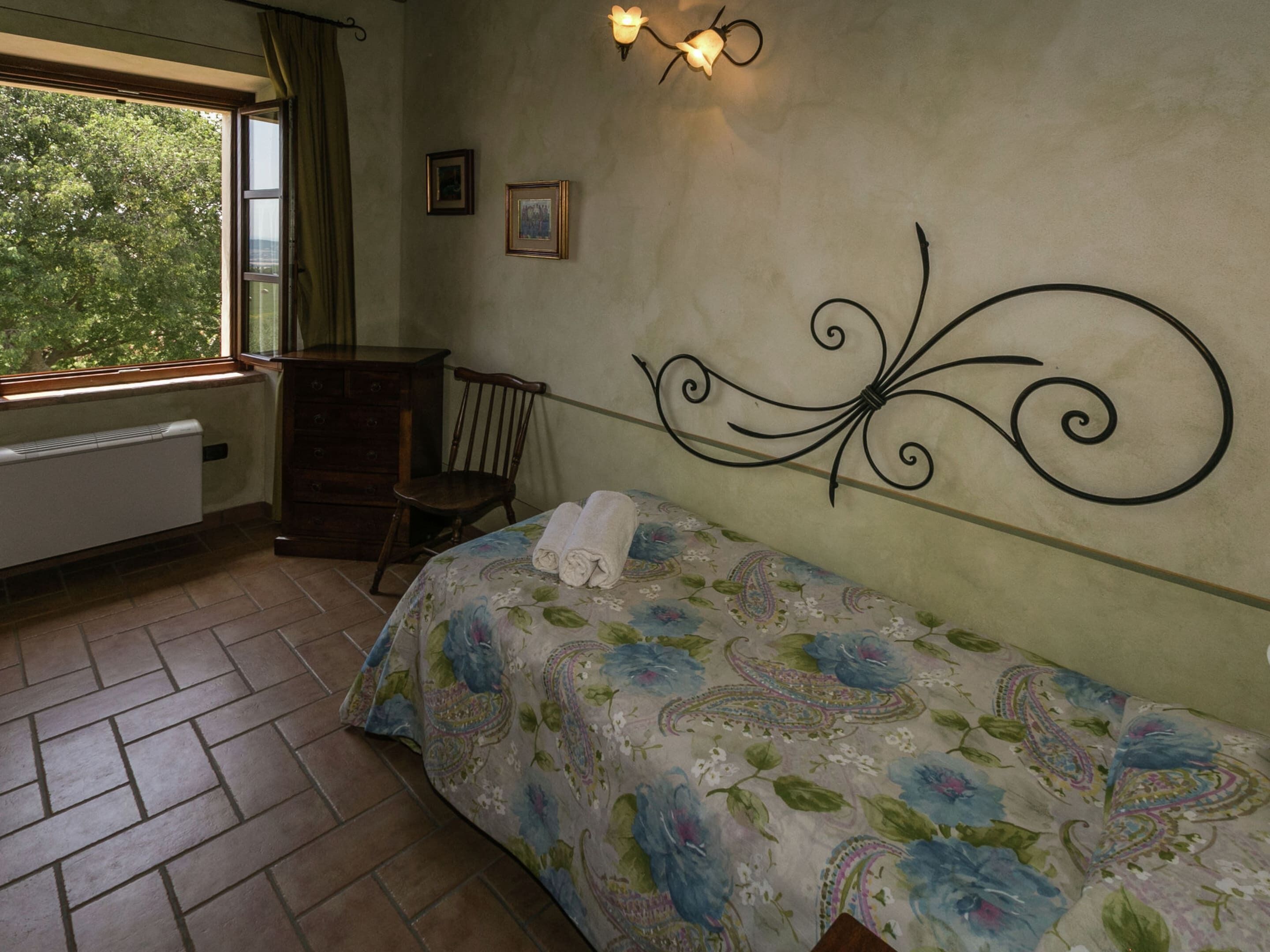 Ein Schlafzimmer mit Bett, Sessel, Heizkörper, Fenster und Wandleuchten.