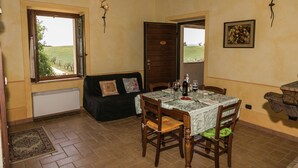Uma área de refeições com uma mesa posta para dois, uma janela com vista para um campo verde e teto de madeira.