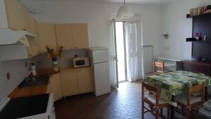 Cocina compacta con lavamanos, microondas y refrigerador. Se observa una mesa de comedor con sillas e iluminación en el techo.