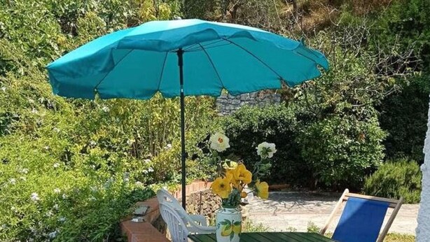 Un patio al aire libre con una sombrilla azul, una mesa con un jarrón de flores y dos sillas.