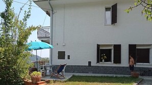 Una casa de dos pisos con balcón, un pequeño jardín y mobiliario exterior.