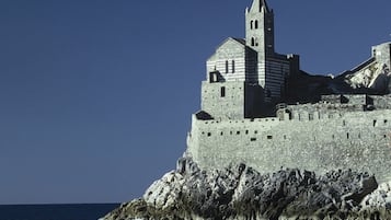 A historic stone castle with a prominent tower, situated on a rocky coastline with the sea in the foreground.