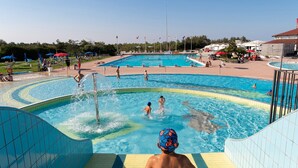 A swimming pool area with multiple pools, a water slide, and people swimming and playing.