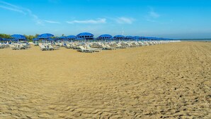 A beach with rows of sun loungers and blue umbrellas under a clear sky.
