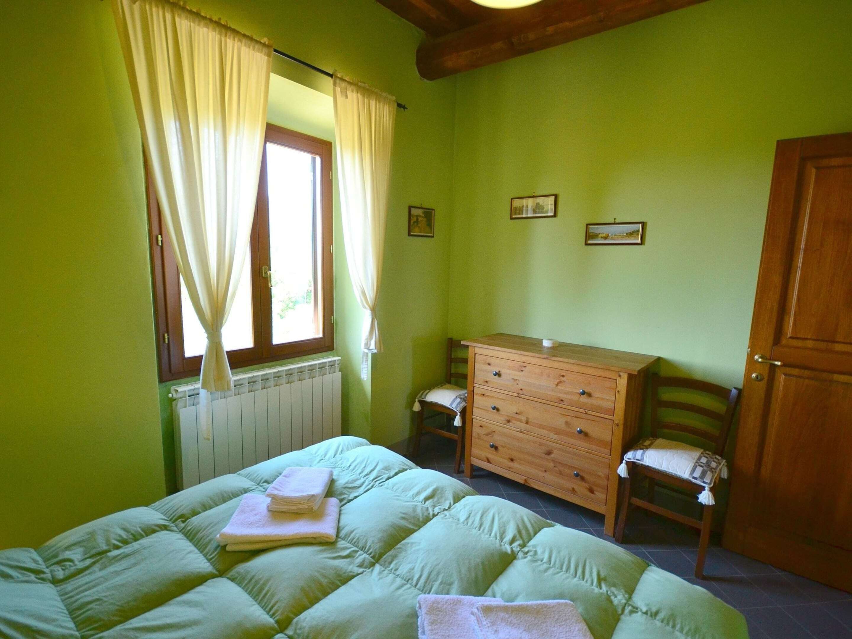 A bedroom with a bed, a wooden dresser, a chair, and a window with curtains.