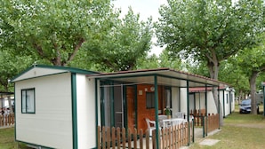A small, single-story mobile home with a covered porch and a fenced outdoor seating area.