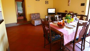 A dining area with a table set for two, a television, and a floral armchair. - Spacious House in Pienza (Pienza)