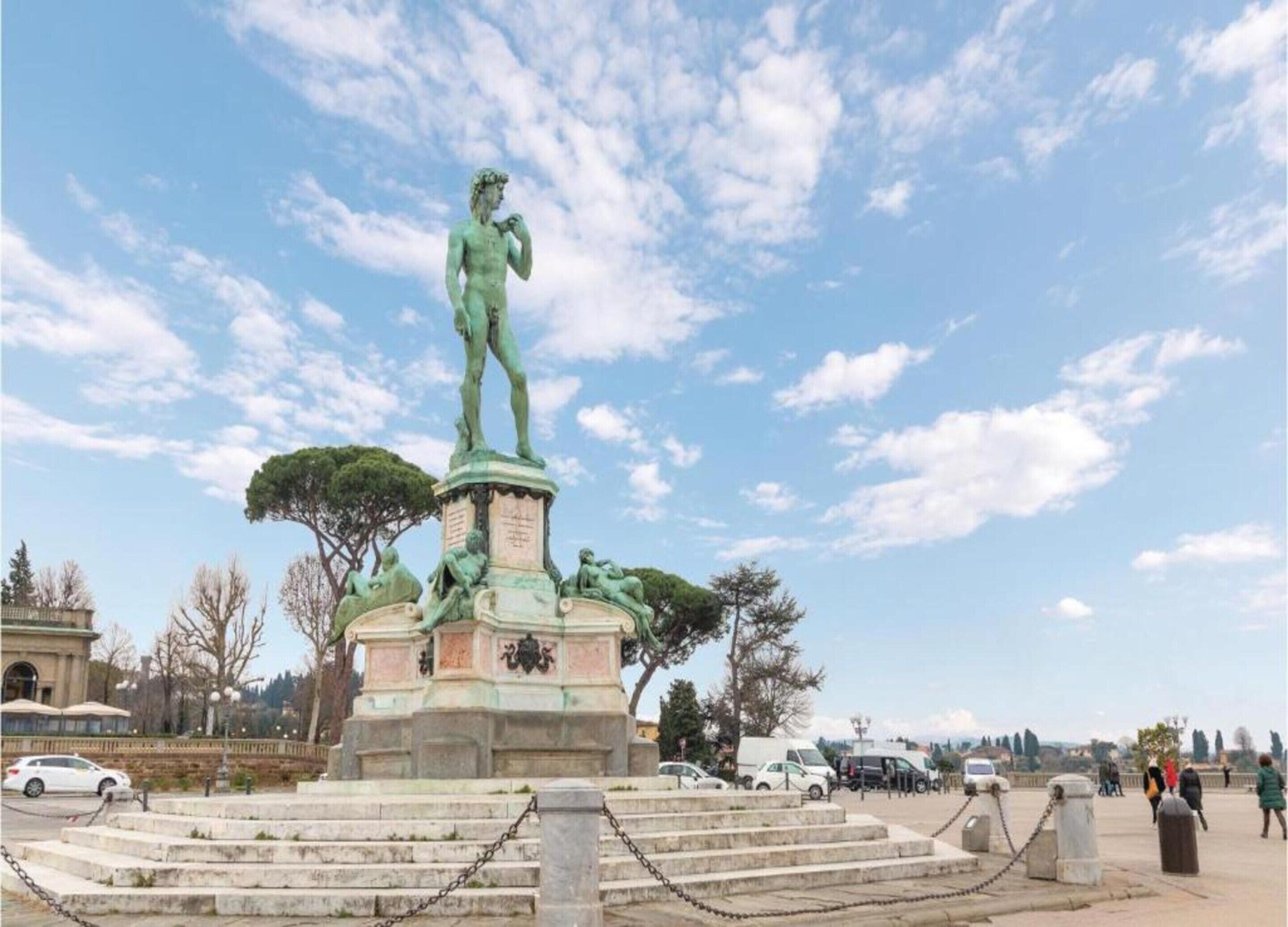 A bronze statue of a standing man on a pedestal with steps leading up to it, surrounded by trees and a clear sky.