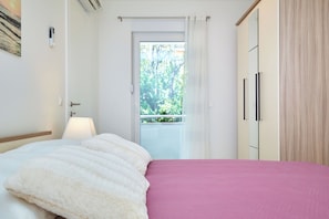 Quarto com cama, mesa de cabeceira, abajur, guarda-roupa e vista para o verde lá fora.