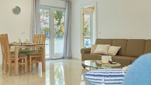 A modern living room with a glass dining table, wooden chairs, a sofa, and a glass coffee table.
