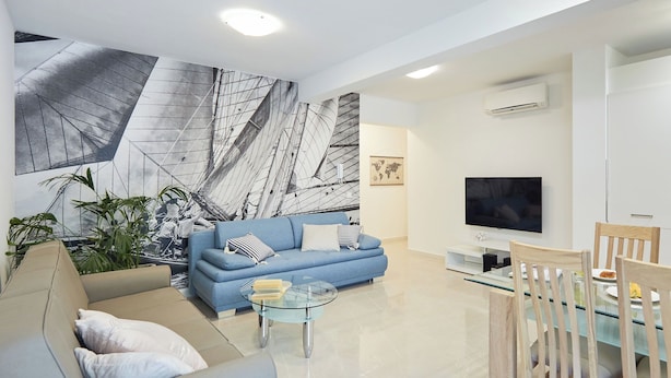 A modern living room with a blue sofa, a glass coffee table, and a dining area with wooden chairs.