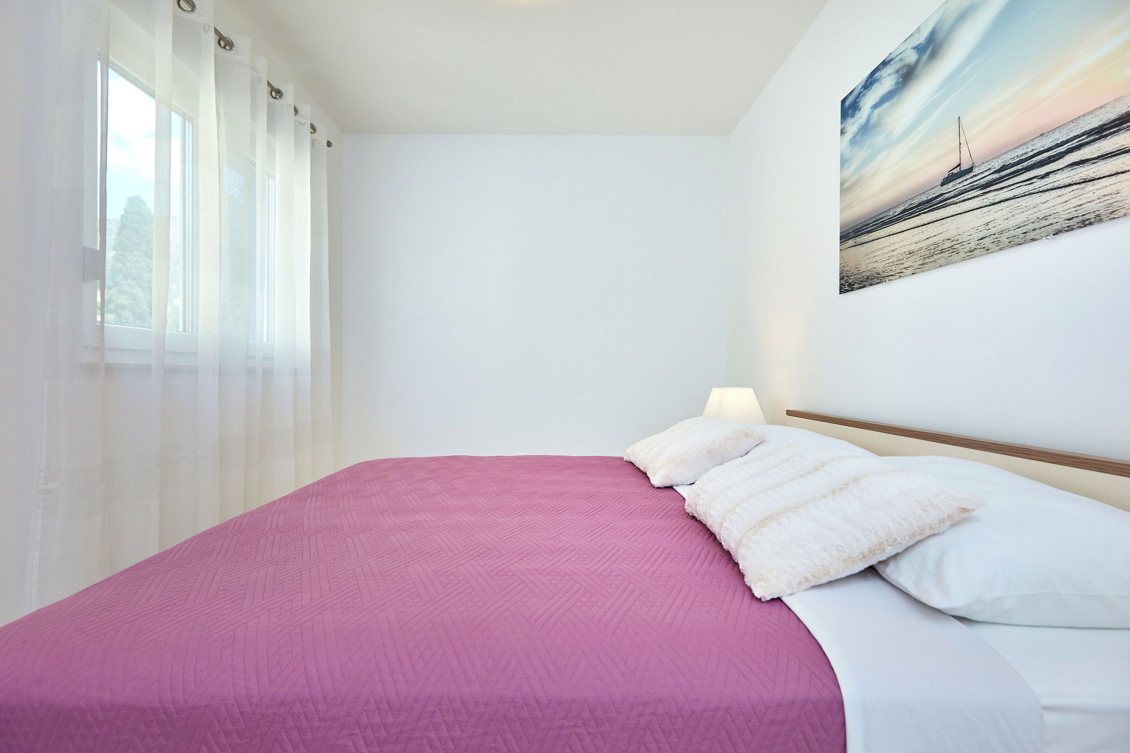 Un dormitorio con cama, cortinas blancas, un cuadro de un velero y una ventana.