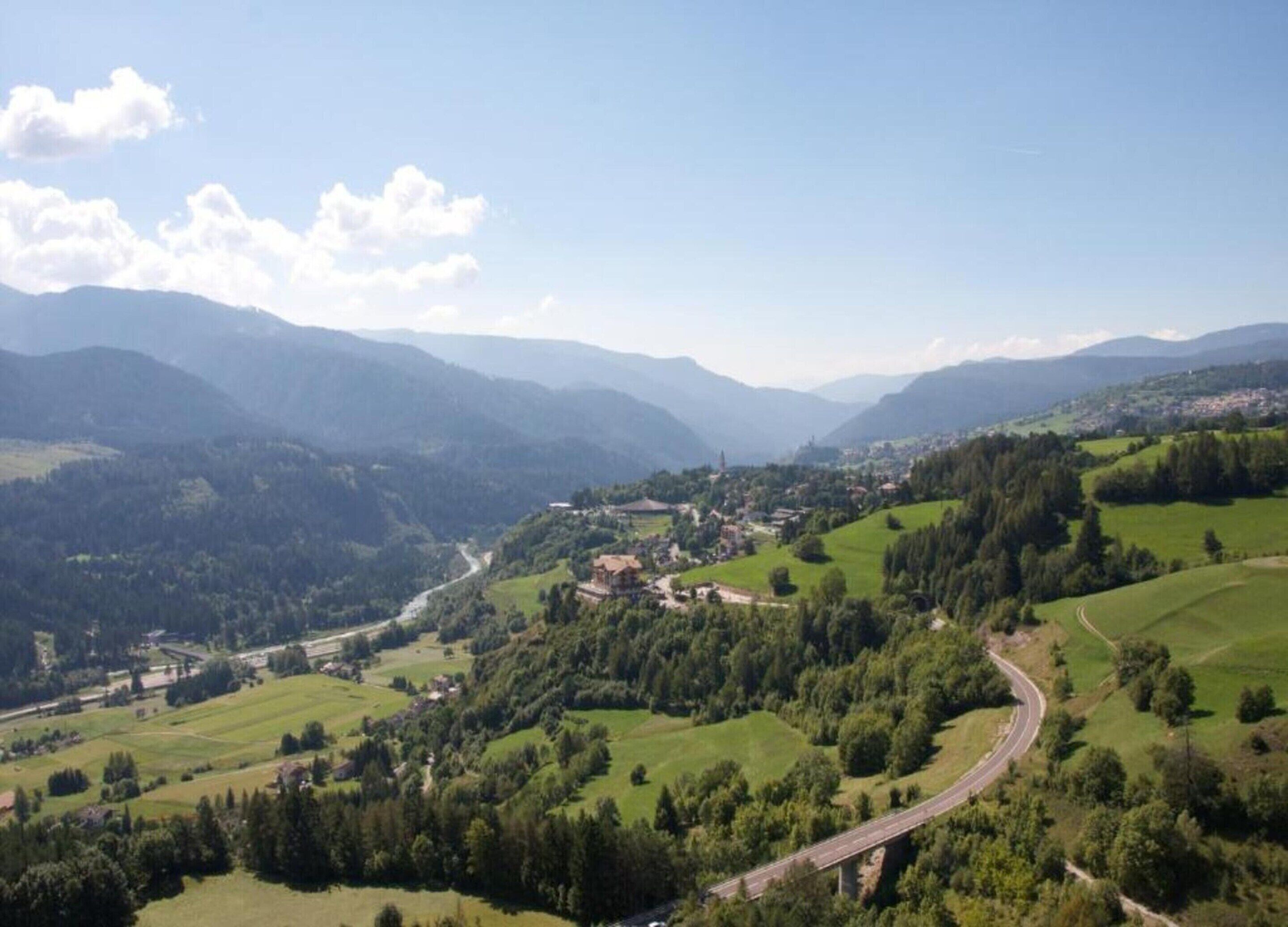 A panoramic view of a valley with a winding road, green fields, and distant mountains.