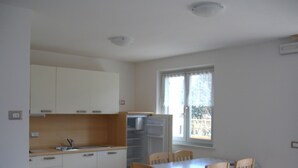 A small kitchen with white cabinets, a sink, and a window. There is a table with chairs and a refrigerator. - Alpine Comfort Stay, Cavalese (Cavalese)