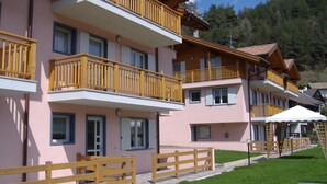 A multi-story hotel with balconies, a covered outdoor seating area, and a well-maintained lawn. - Alpine Comfort Stay, Cavalese (Cavalese)