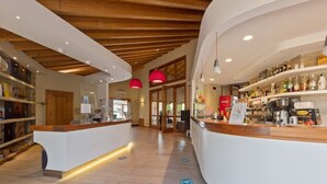 Un bar moderne avec des poutres en bois au plafond, un comptoir où sont exposées différentes bouteilles et un espace détente agrémenté d’une lampe rouge.
