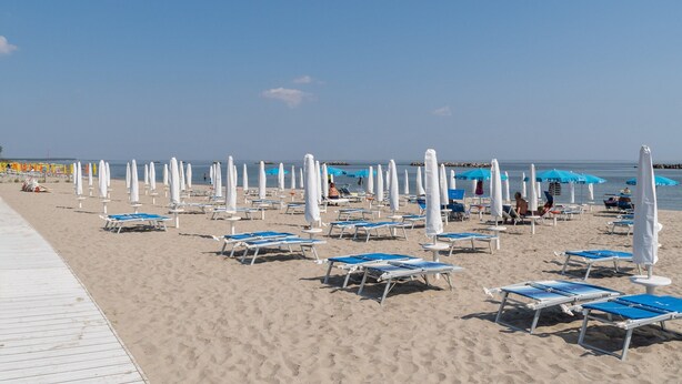 Une plage bordée de rangées de chaises longues et de parasols, une promenade en bois et un ciel bleu azur.