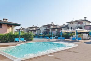 A pool area with lounge chairs and umbrellas, surrounded by buildings with tiled roofs. - Sunny Coastal Escape in Lido (Comacchio)