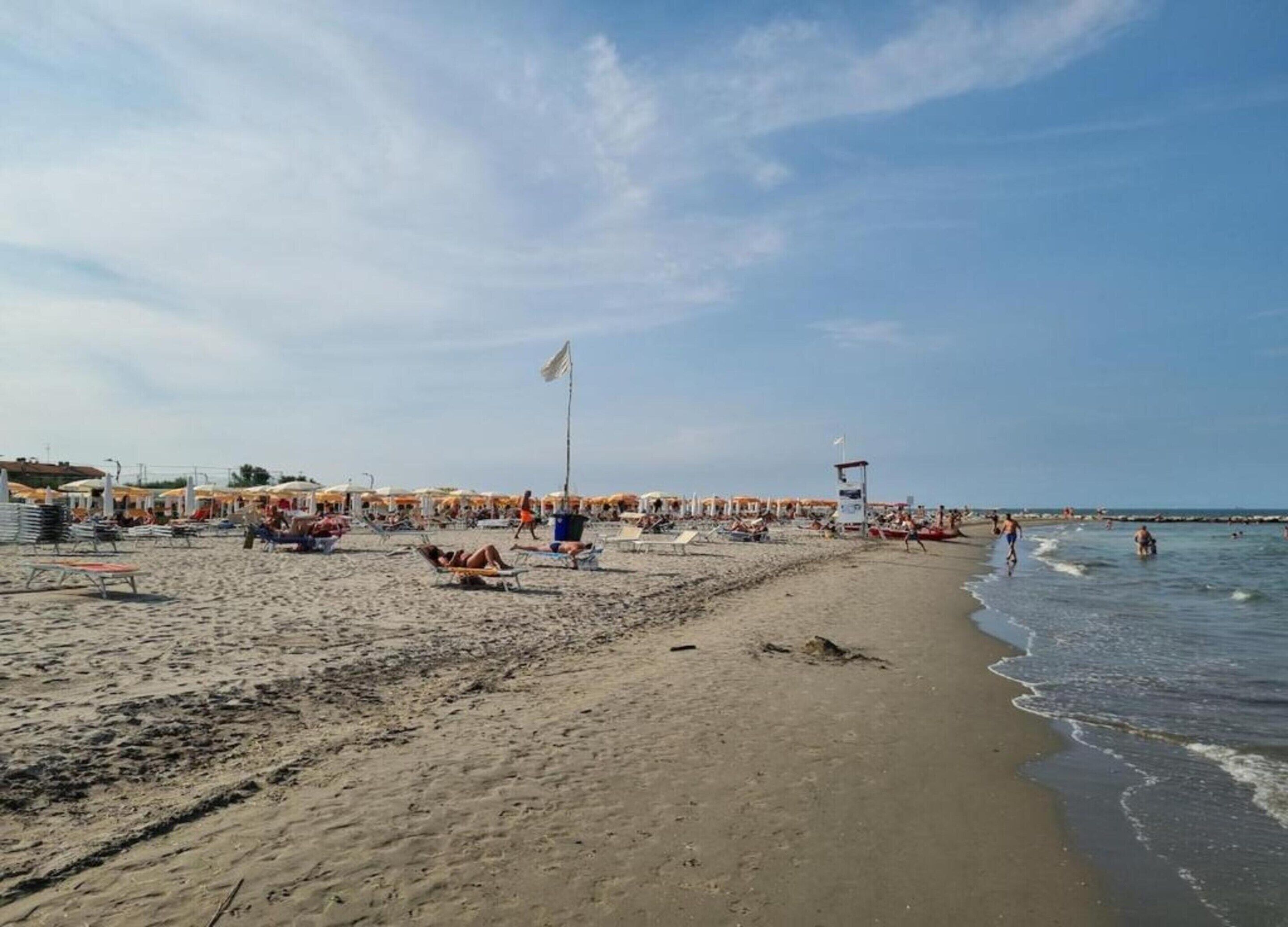 A beach with sun loungers and umbrellas, a lifeguard tower, and a clear sky.