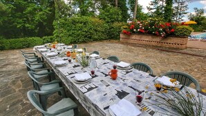 An outdoor dining area with a long table set for a meal, surrounded by greenery and a brick planter with flowers. - _x000d_
boutique Villa With Pool (Anghiari)