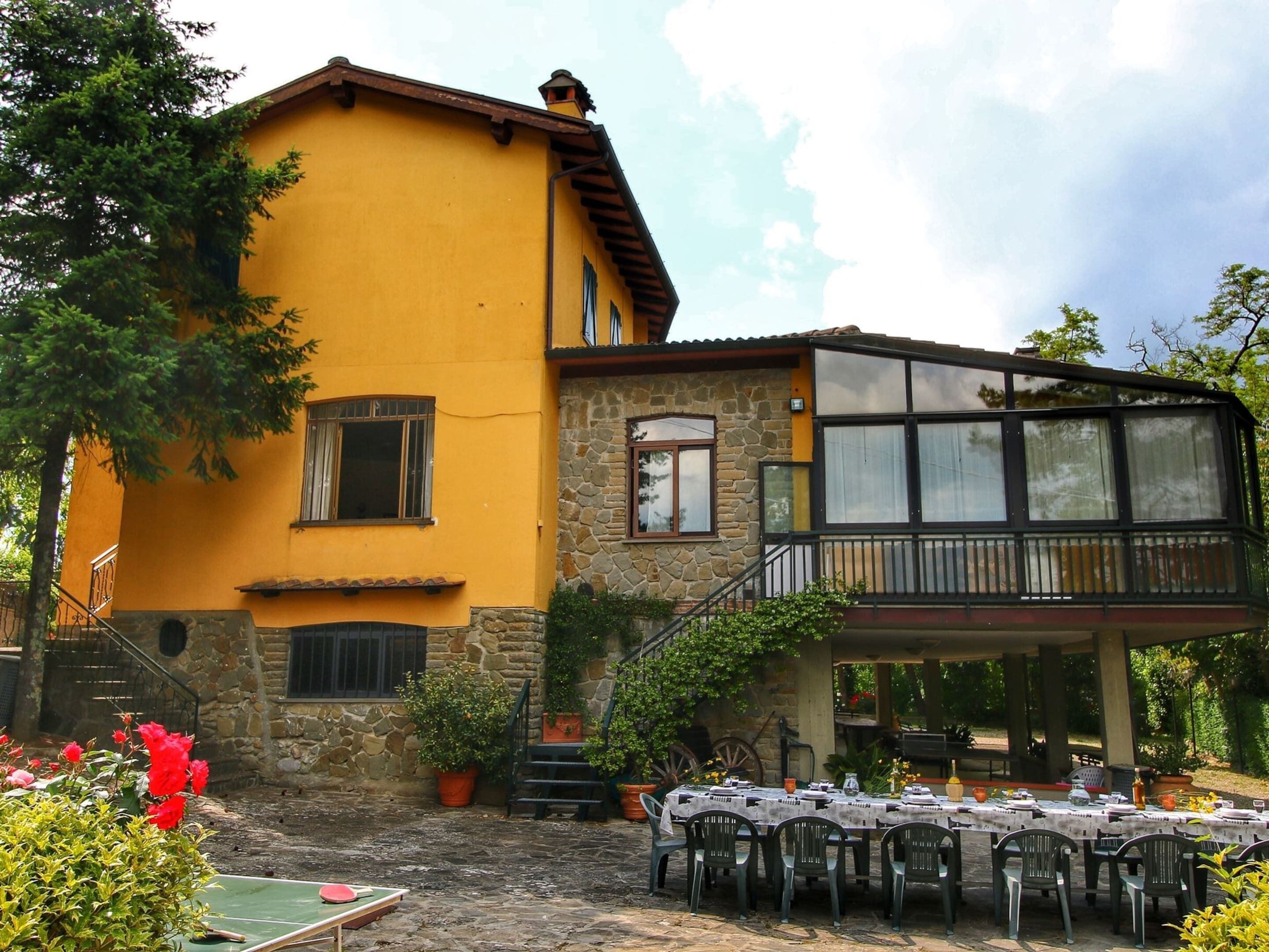 A yellow building with a stone facade, a balcony with a wooden railing, and outdoor tables set up for dining.