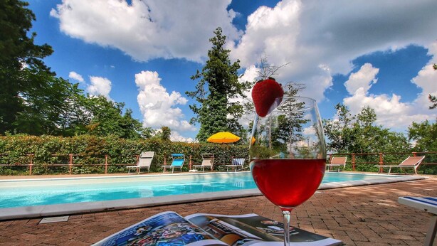 A glass of red drink with a strawberry on the rim, an open magazine, and a poolside setting with lounge chairs and umbrellas. - _x000d_
boutique Villa With Pool (Anghiari)