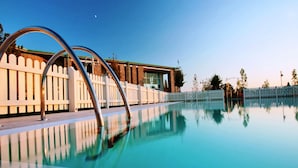 A clear swimming pool with a metal ladder, surrounded by a white fence and a building with a green roof. - Apartment in Chianti With Shared Pool (Barberino Tavarnelle)