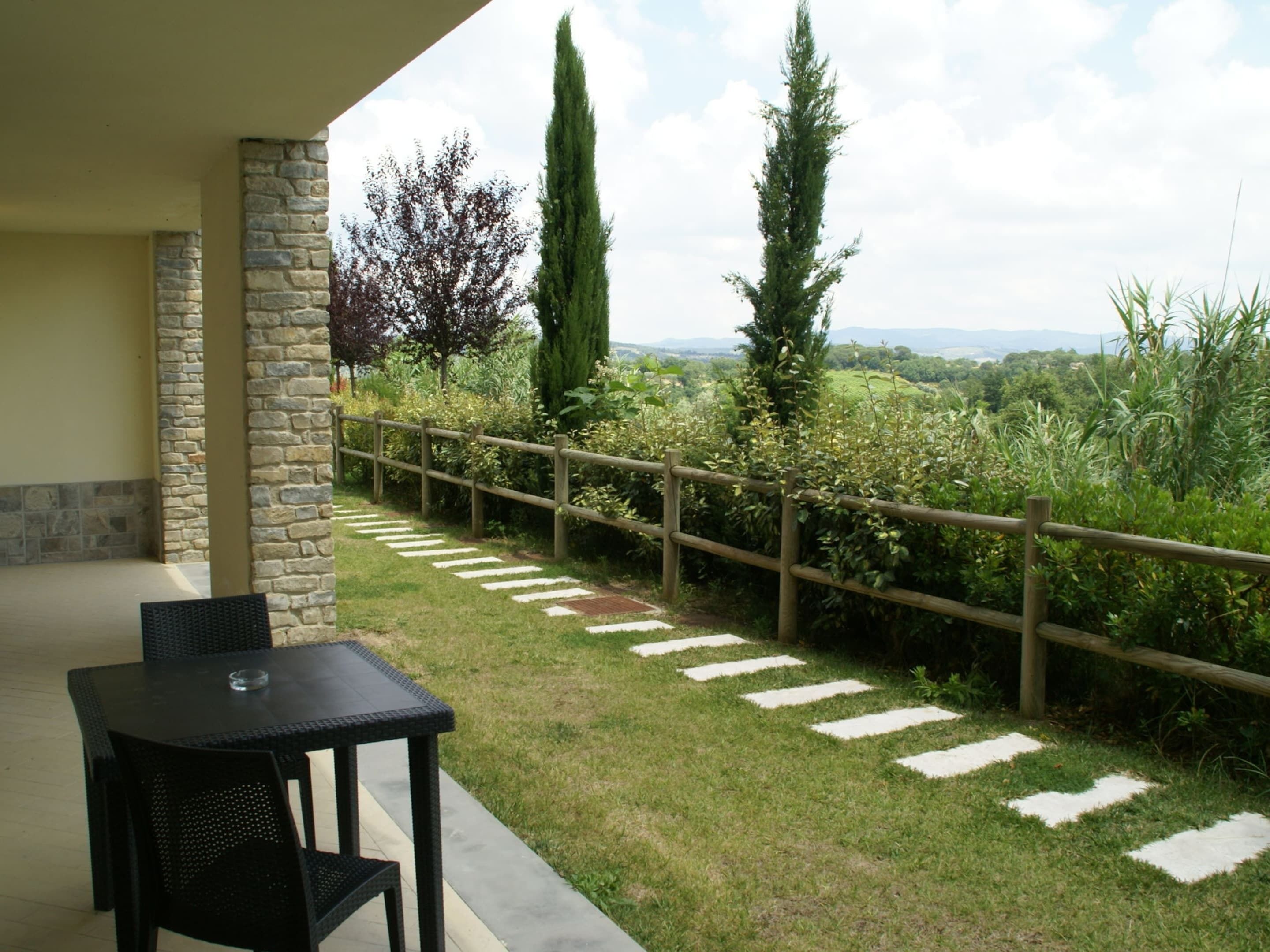 A patio with a stone wall, a wooden fence, and a view of a grassy landscape with trees.