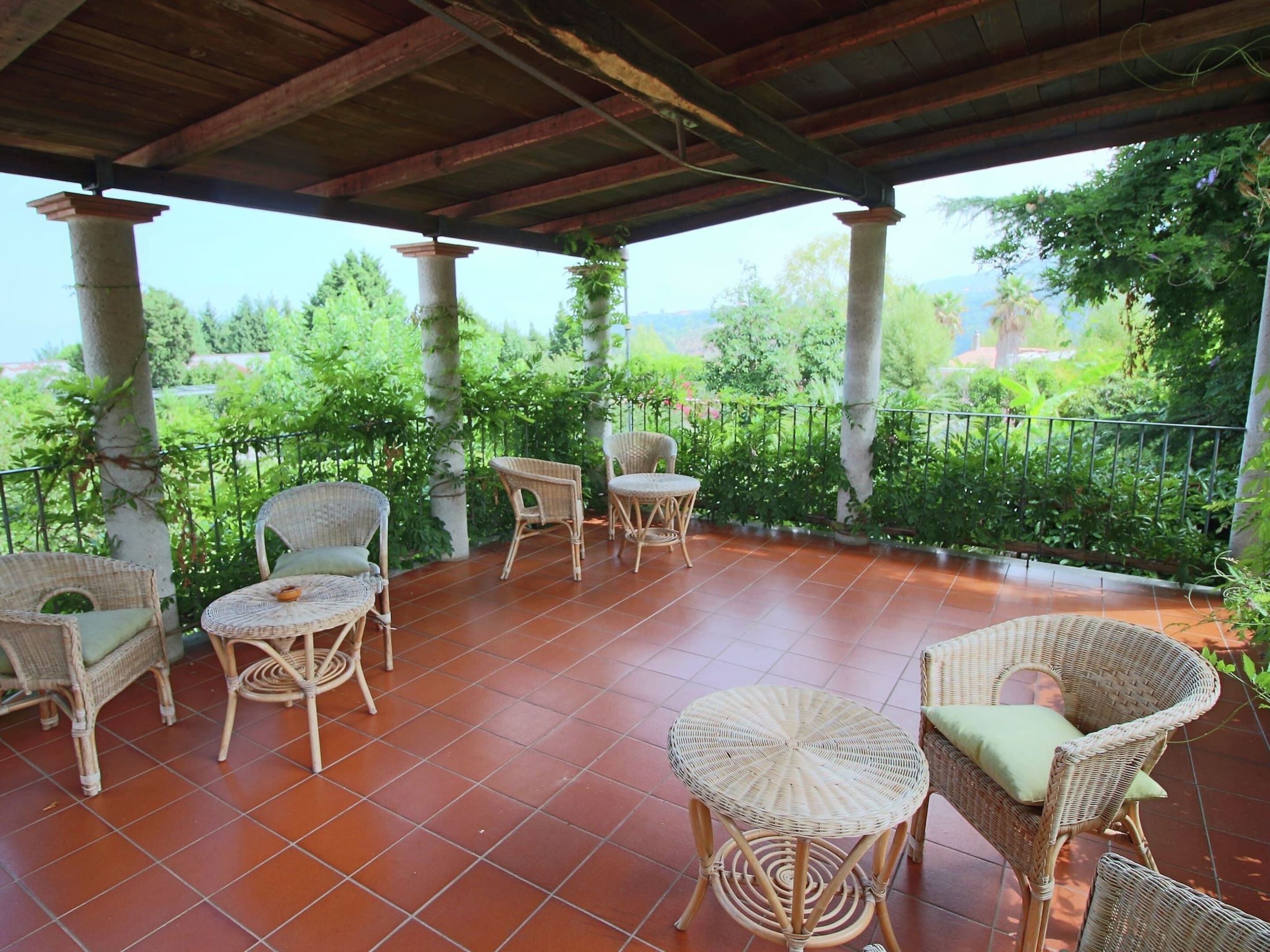 A covered patio with wicker furniture and a view of greenery.