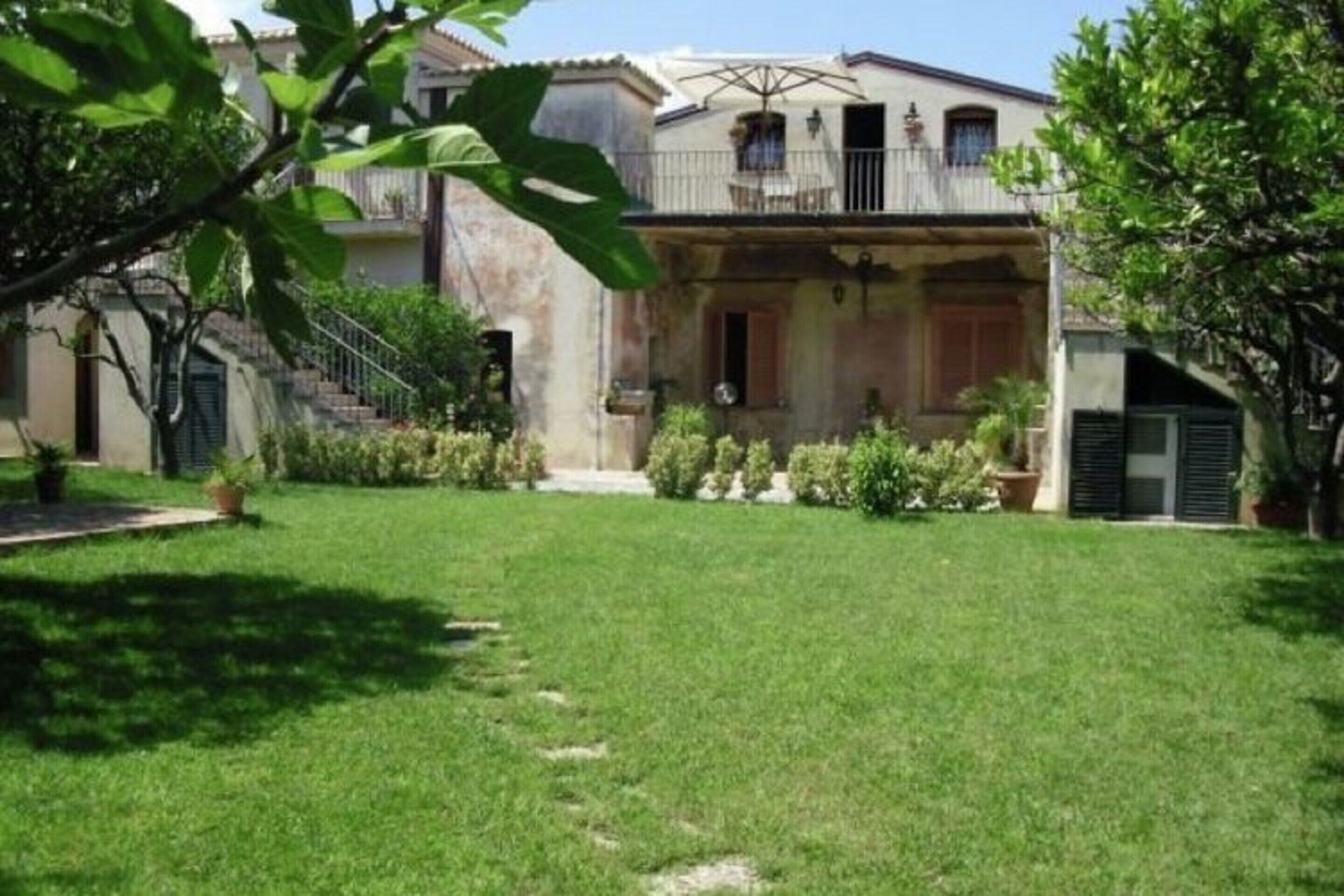 Una casa de dos pisos con balcón, césped cuidado y plantas en macetas.