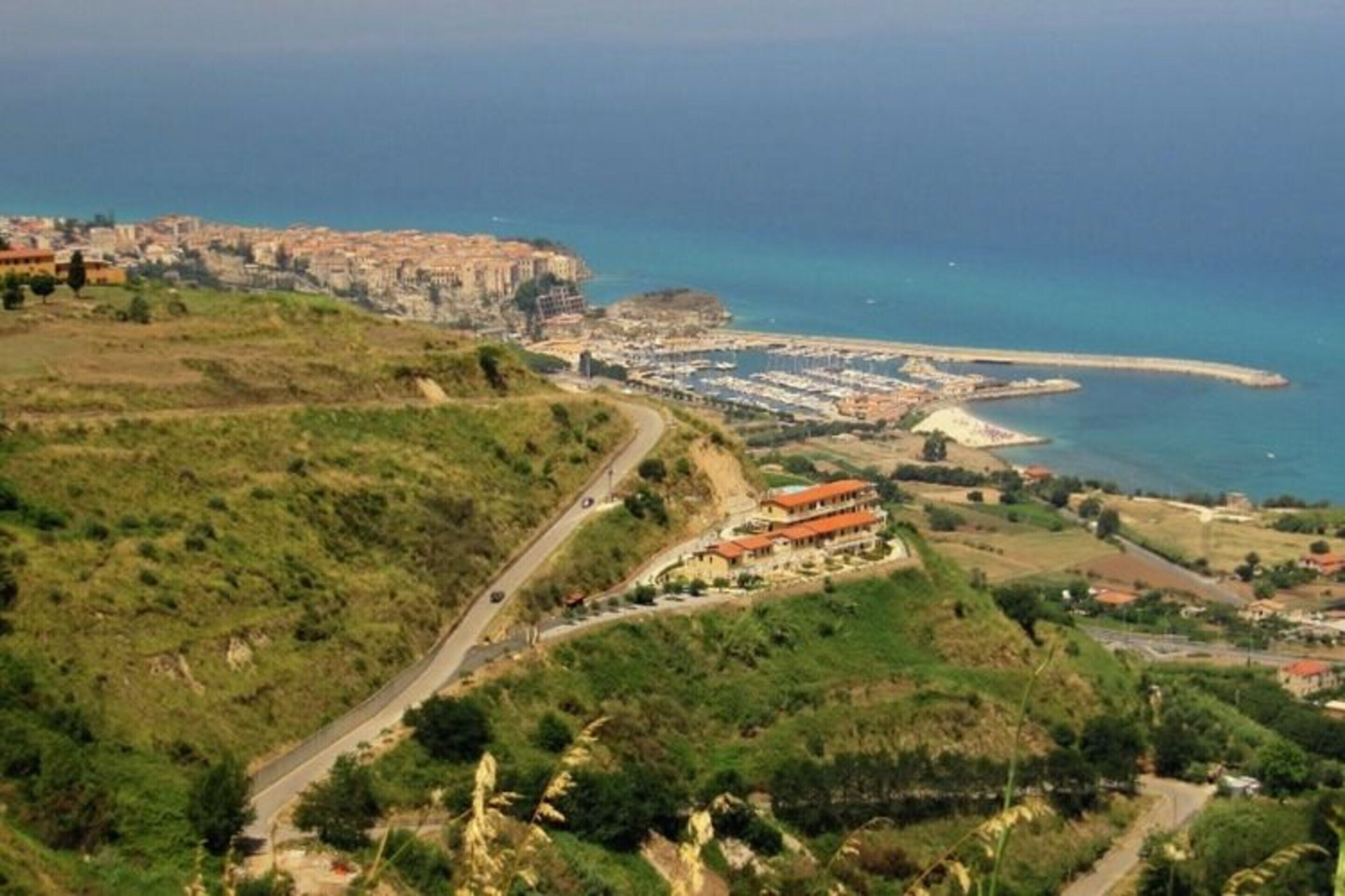 A coastal town with a prominent building on a hill, a marina, and a winding road.
