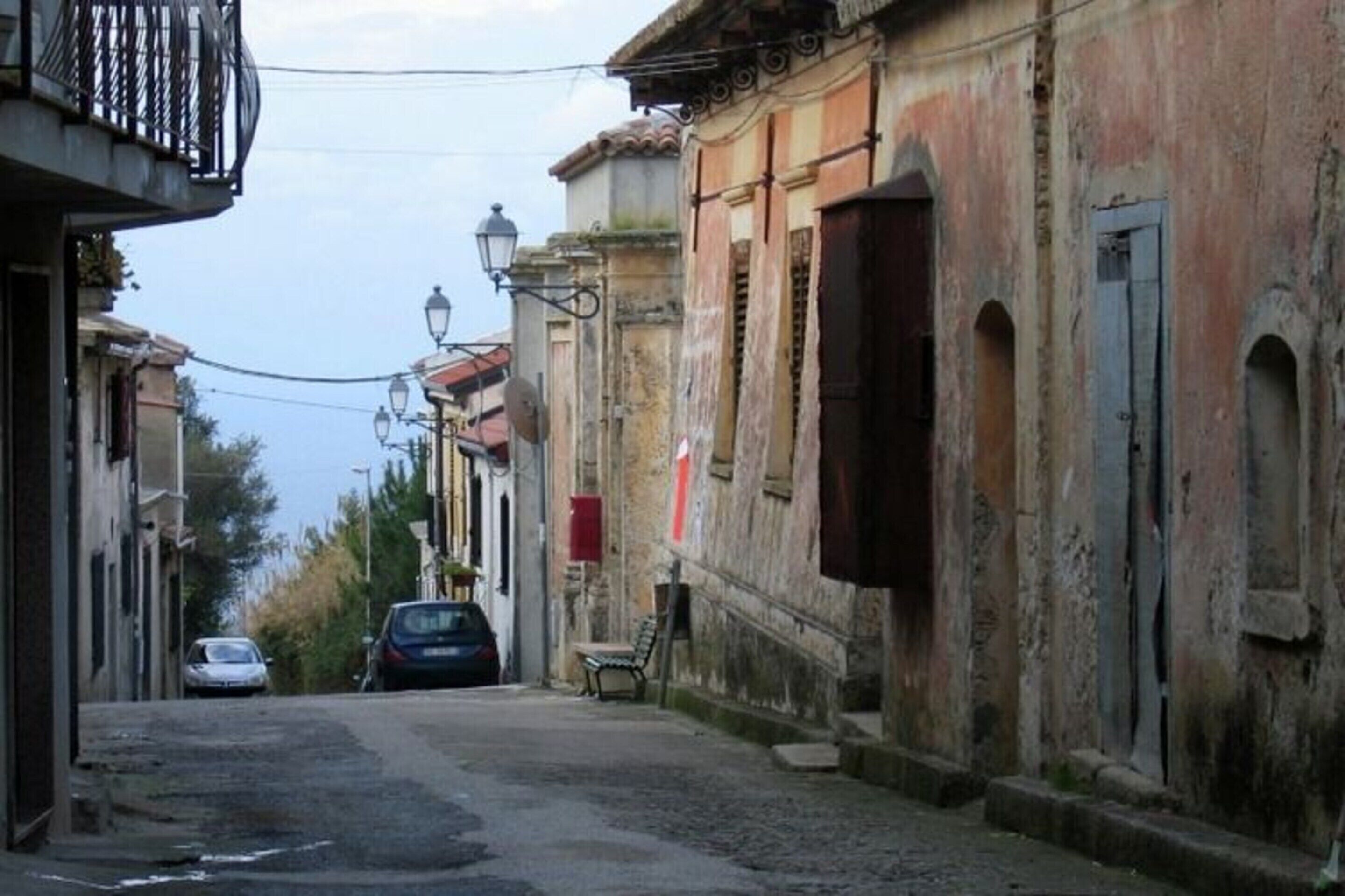 A narrow street with historic buildings, a bench, and a car parked on the side.