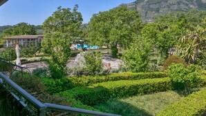 A lush garden with a variety of trees and shrubs, a stone pathway, and a building with a blue roof in the background. - Holiday Home in San Cipriano With Pool (San Cipriano Picentino)